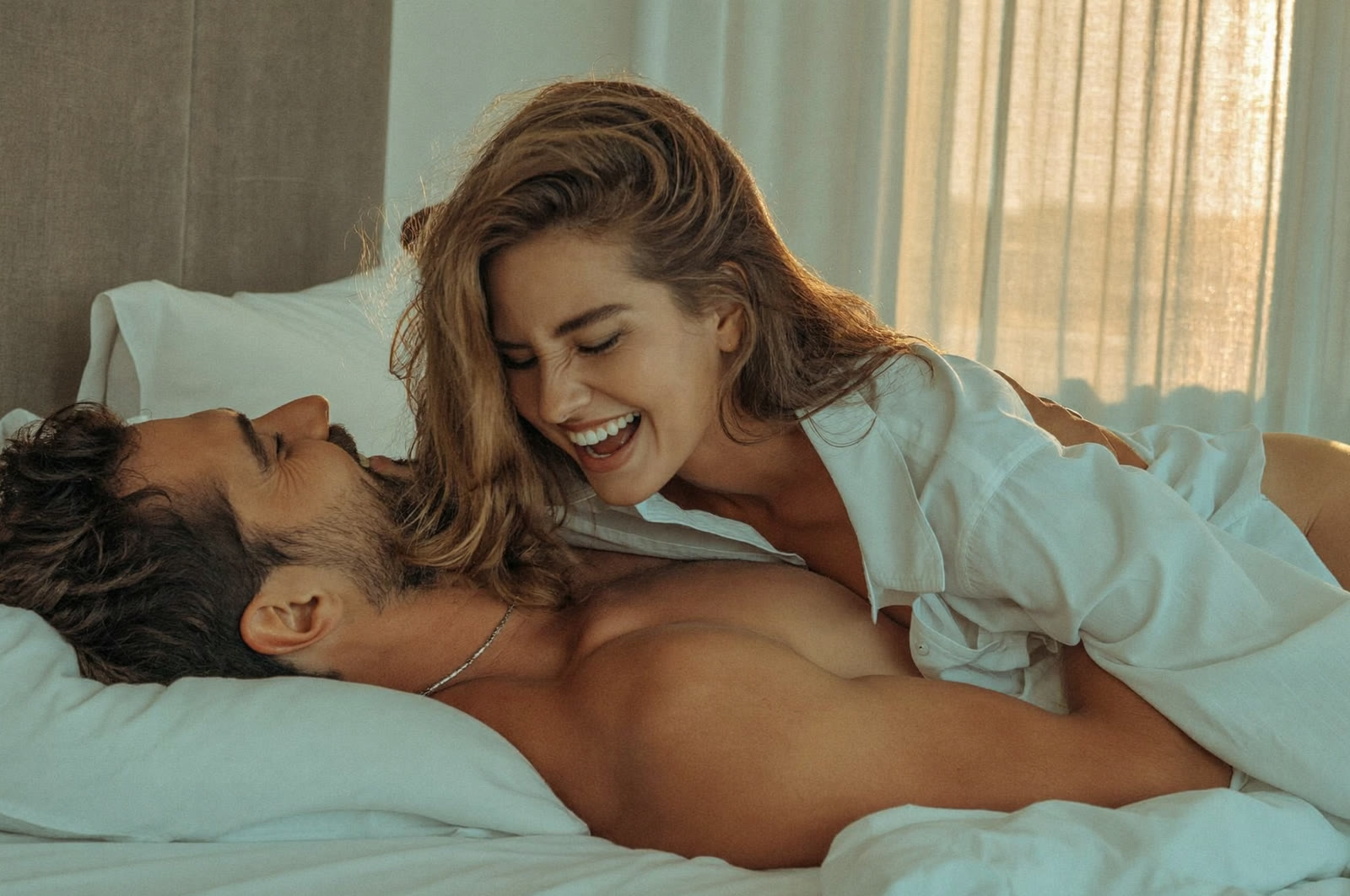A smiling couple together in bed in soft morning light