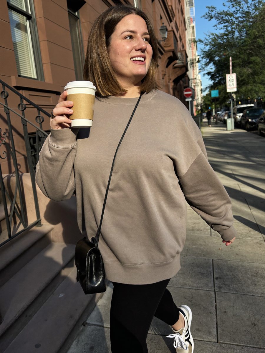 Woman walking down a city sidewalk holding a coffee cup