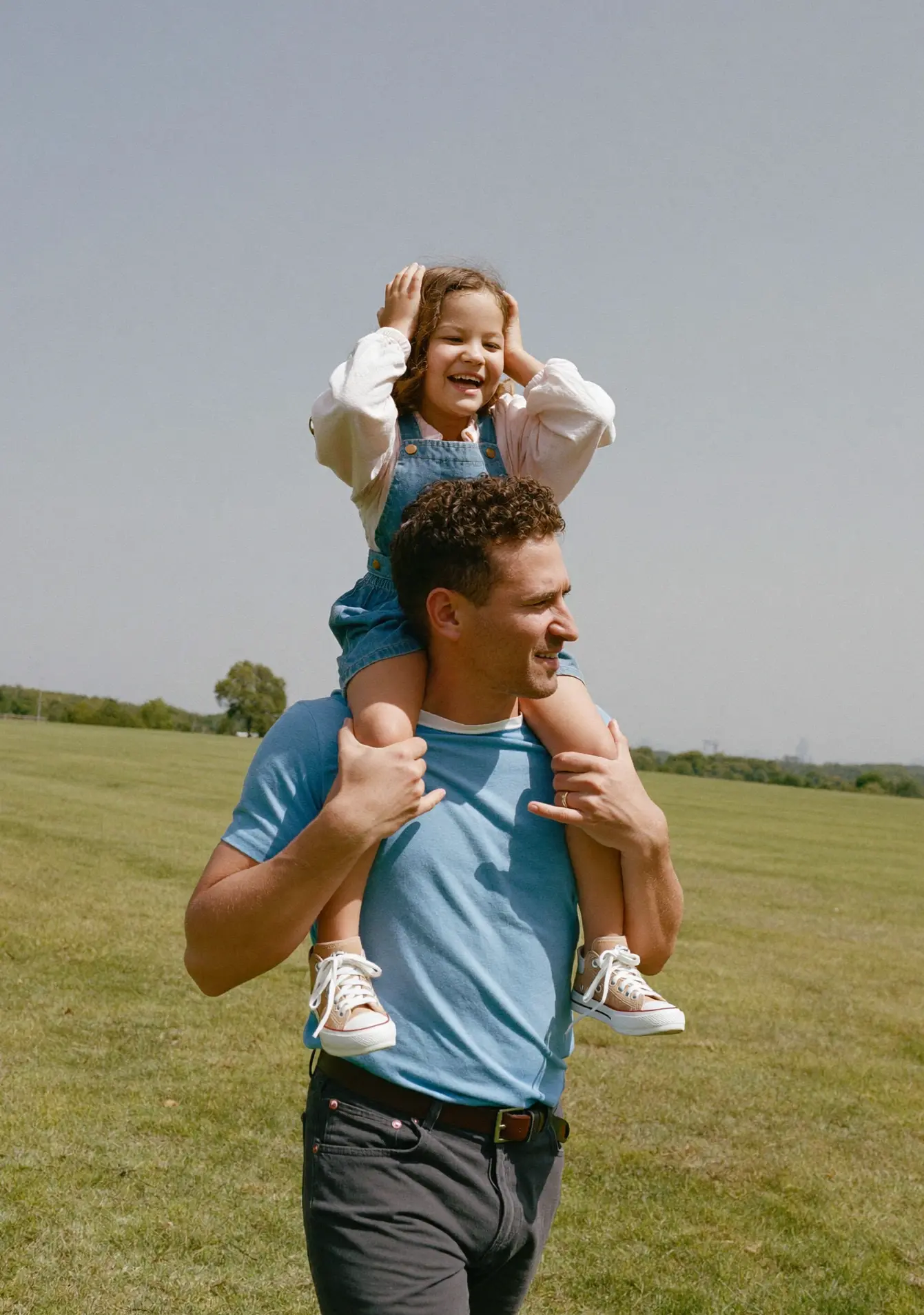 A father carrying his daughter on his shoulders in a sunlit field