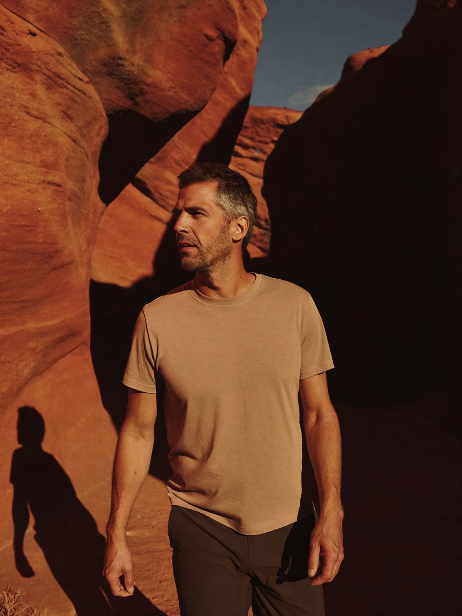 Man in a tan t-shirt walking past a sunlit red rock wall